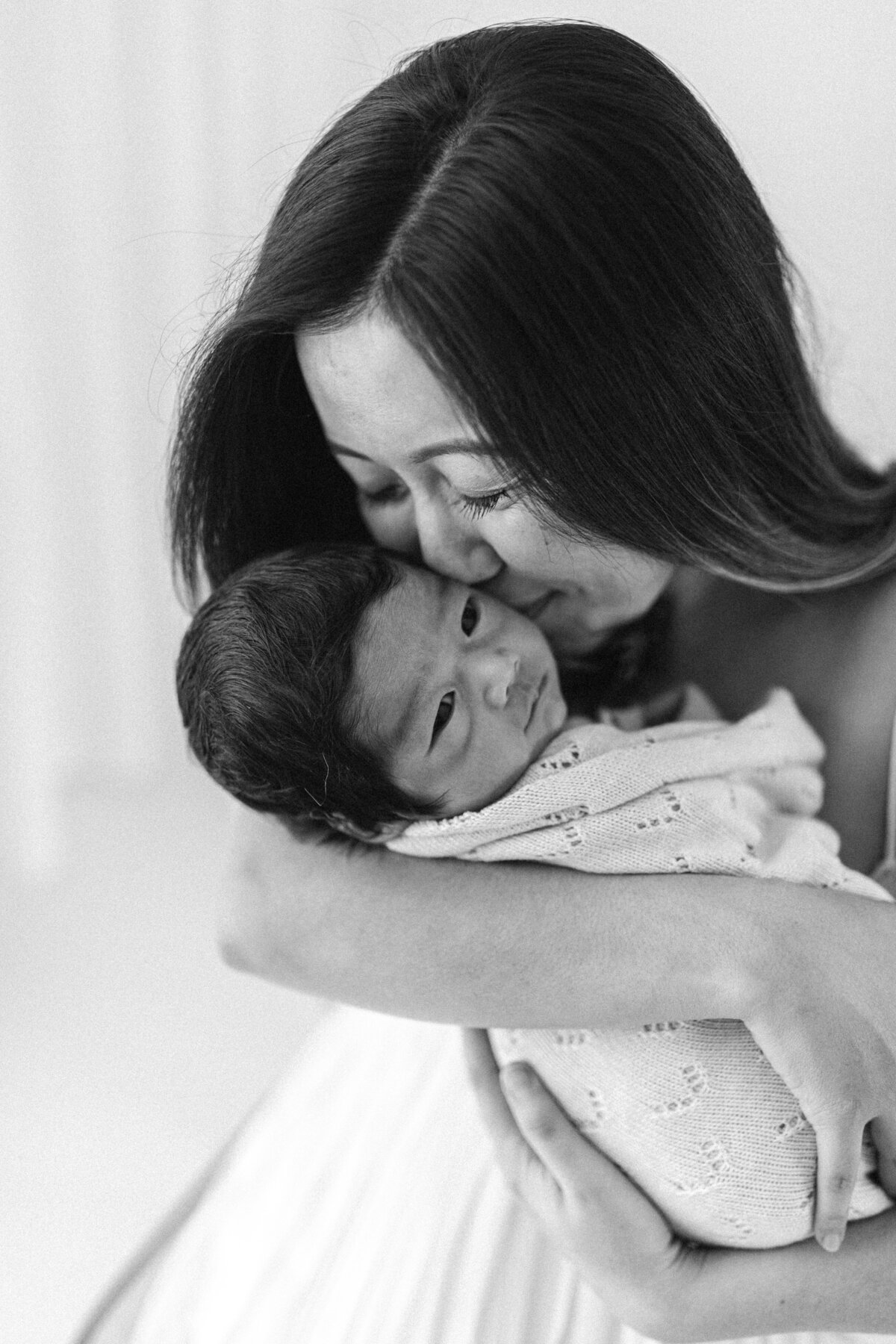 Mum kisses newborn baby black and white photo