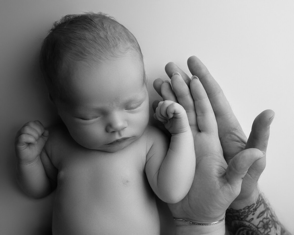 Black and white image of baby’s hand resting next to tattooed parent's hand | Newborn detail photo in Georgetown and Austin, TX