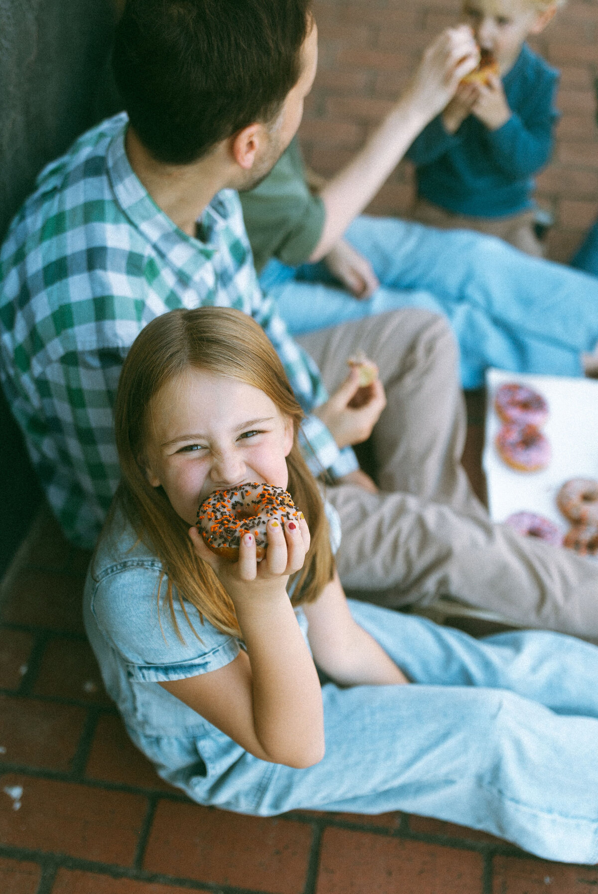 A young girl eating a chocolate glazed donut with sprinkles. 