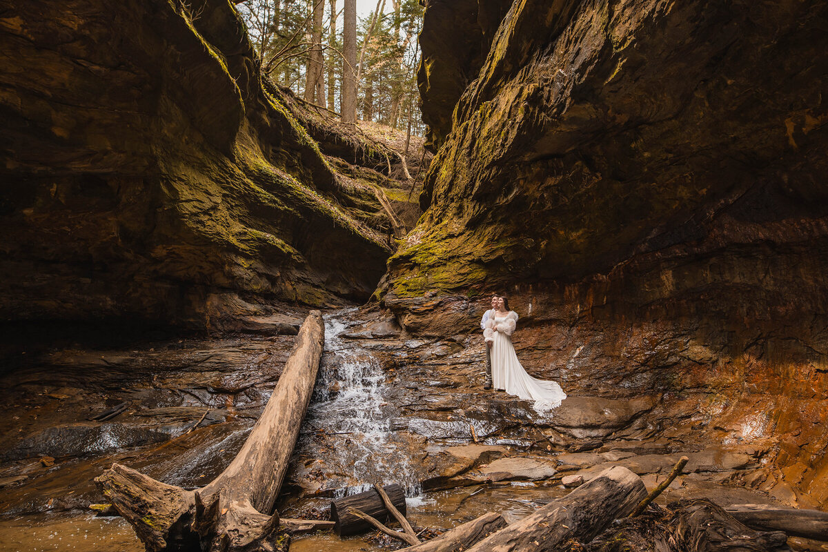 Couple holds each other close standing in a gorge next to a waterfall in Indiana.