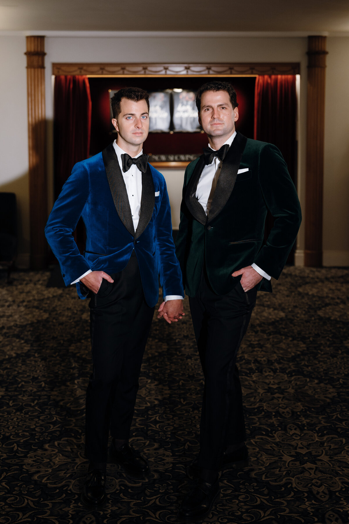 Two grooms posing inside the Regal Cinema for their wedding, a spotlight shining on them.