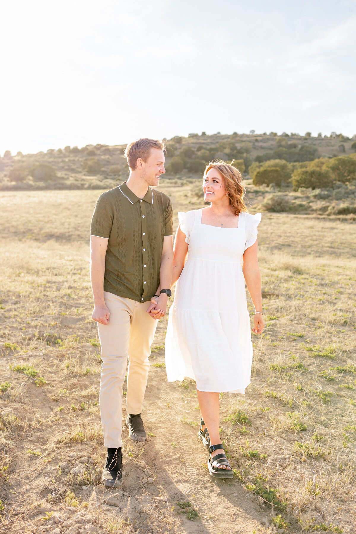Fun and young couple smiling joyfully into one anothers eyes as they walk hand in hand through the desert.