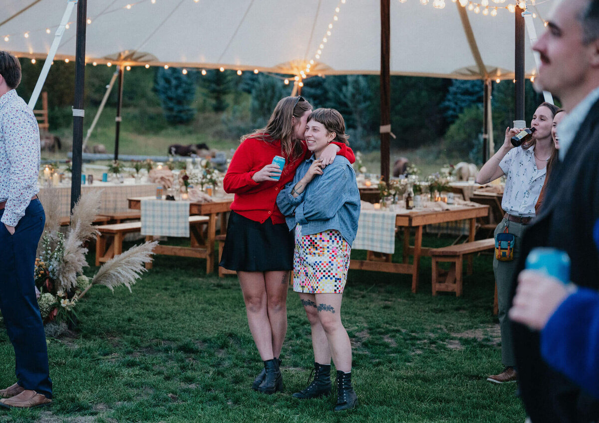 Wedding guests embracing at and outdoor wedding reception on the grass with stringed lights behind them. 