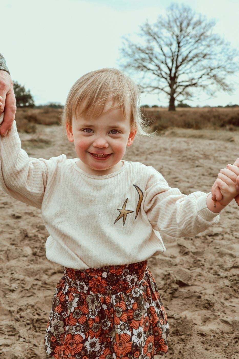 Kinderfoto buiten. Portret van een jong meisje met bloemenprint rok en sterretje op trui. Vrolijk kind in natuurlijk landschap