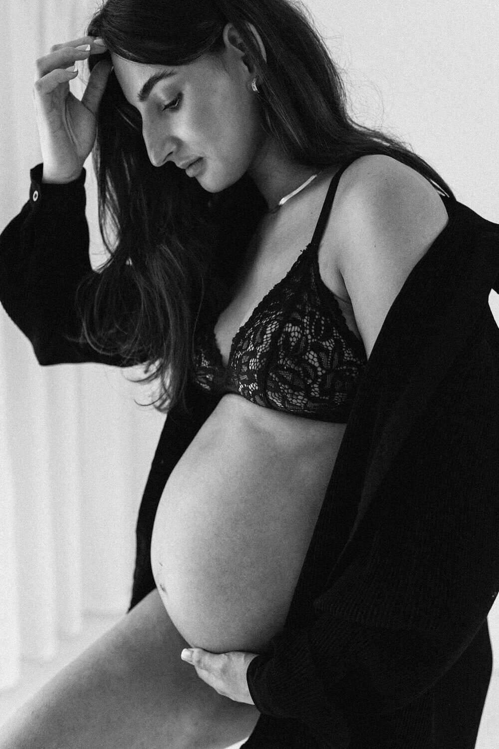 pregnant woman wearing black underwear and a black shirt holds her bump and looks down whilst tucking her hair back