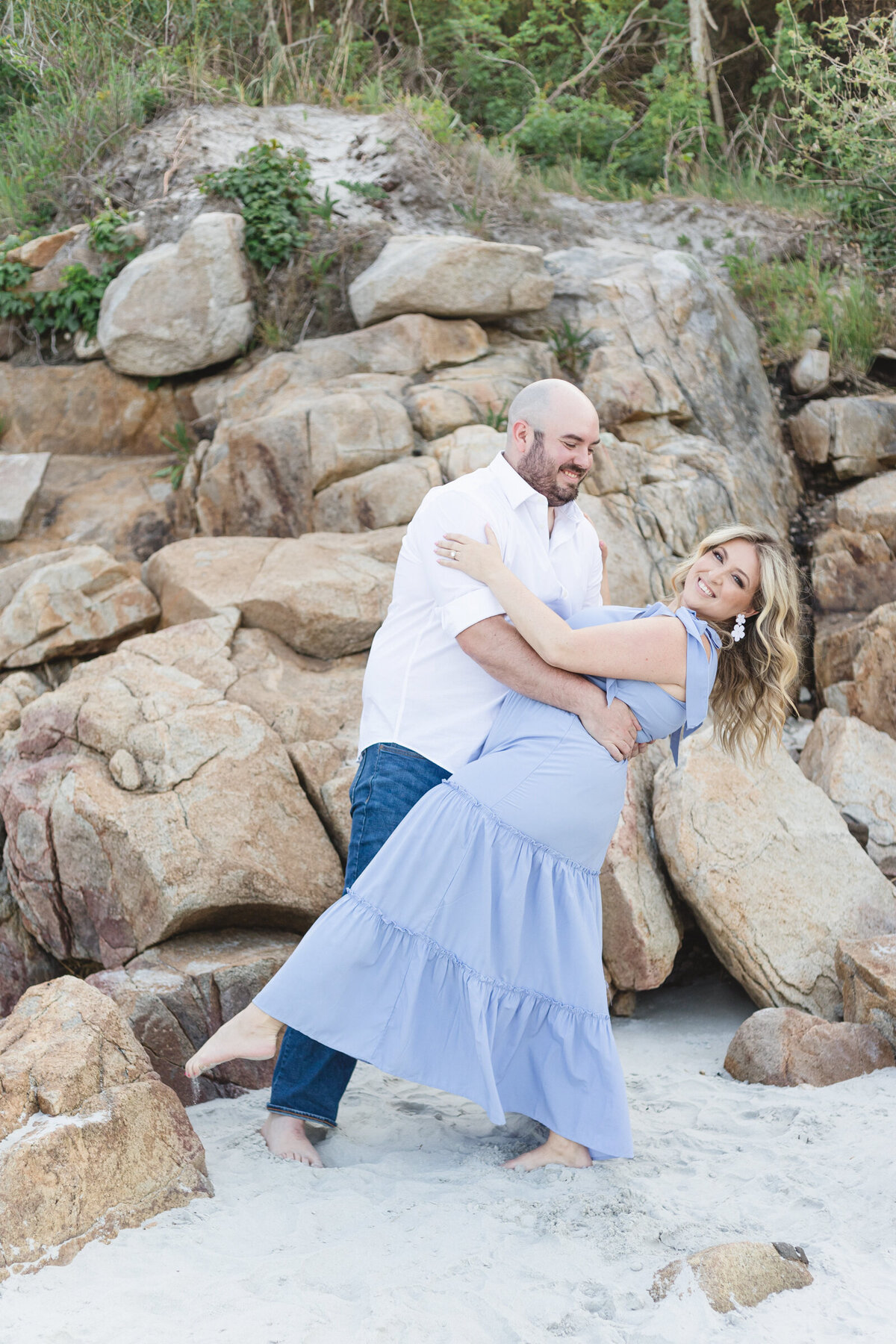 A man dips his fiancee as they dance on the beach