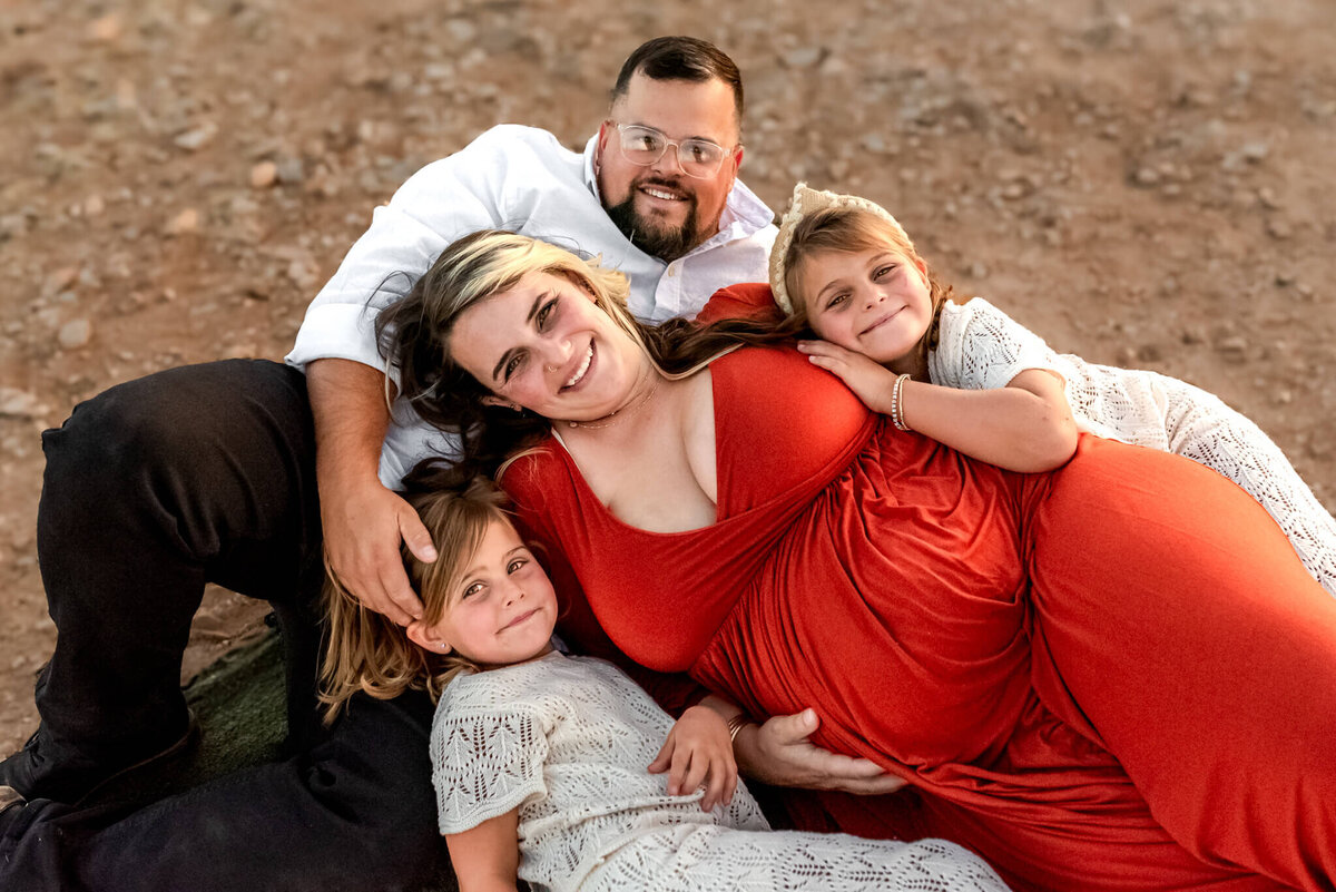 Family lying together on blanket in the desert during maternity photos. Captured by Arizona photographer
