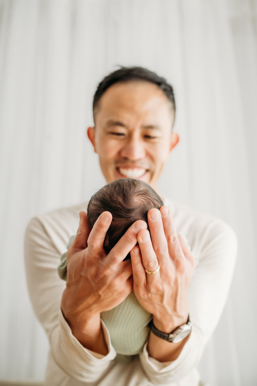 newborn boy in dads hands. his head in in dads heands and you can see dad smiling down at the baby