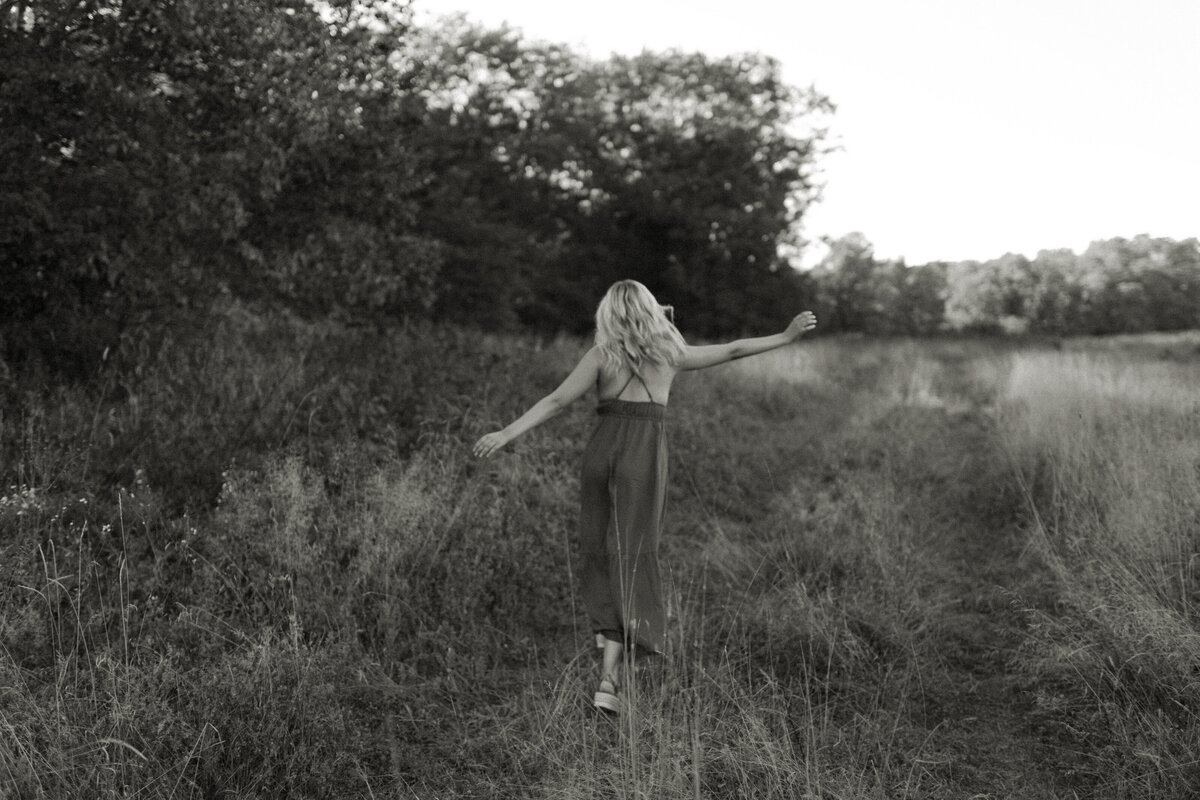 A Northern Wisconsin senior frolics along a dirt path among tall grasses during a midwestern Summer senior session, captured by Emmie Verdell Photo.