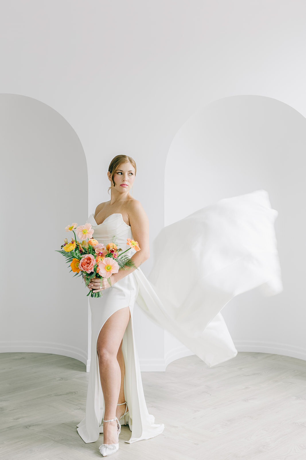 A bride holding a colourful bouquet poses while her train flows behind her.