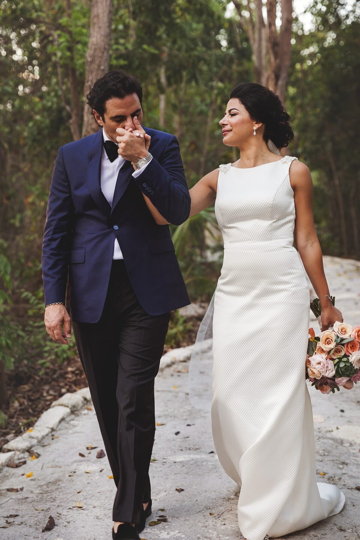 Groom kisses brides hand as they walk down path in Riviera Maya