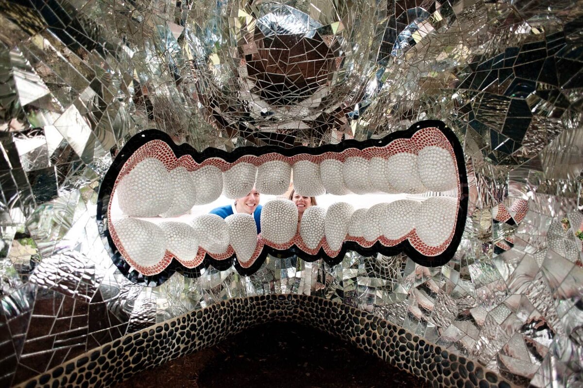 a funny couple show their pearly whites while looking through a sculpture of teeth