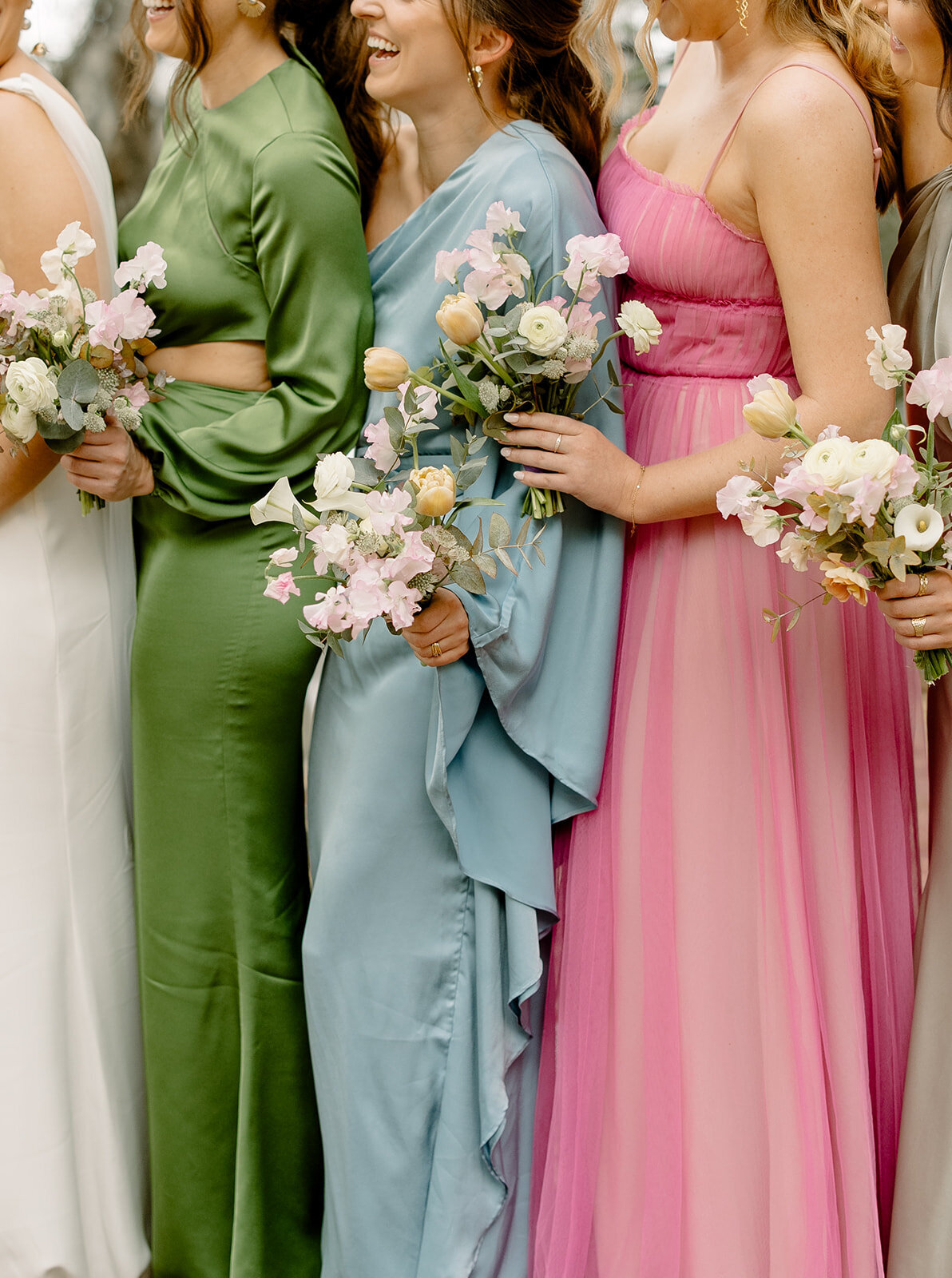 Bridesmaids holding light bouquets and all wearing different color dresses