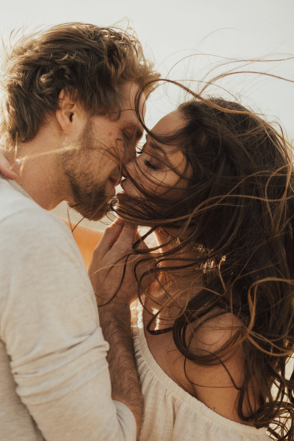 photo of a couple kissing and the wind is blowing the womans hair beautifully.