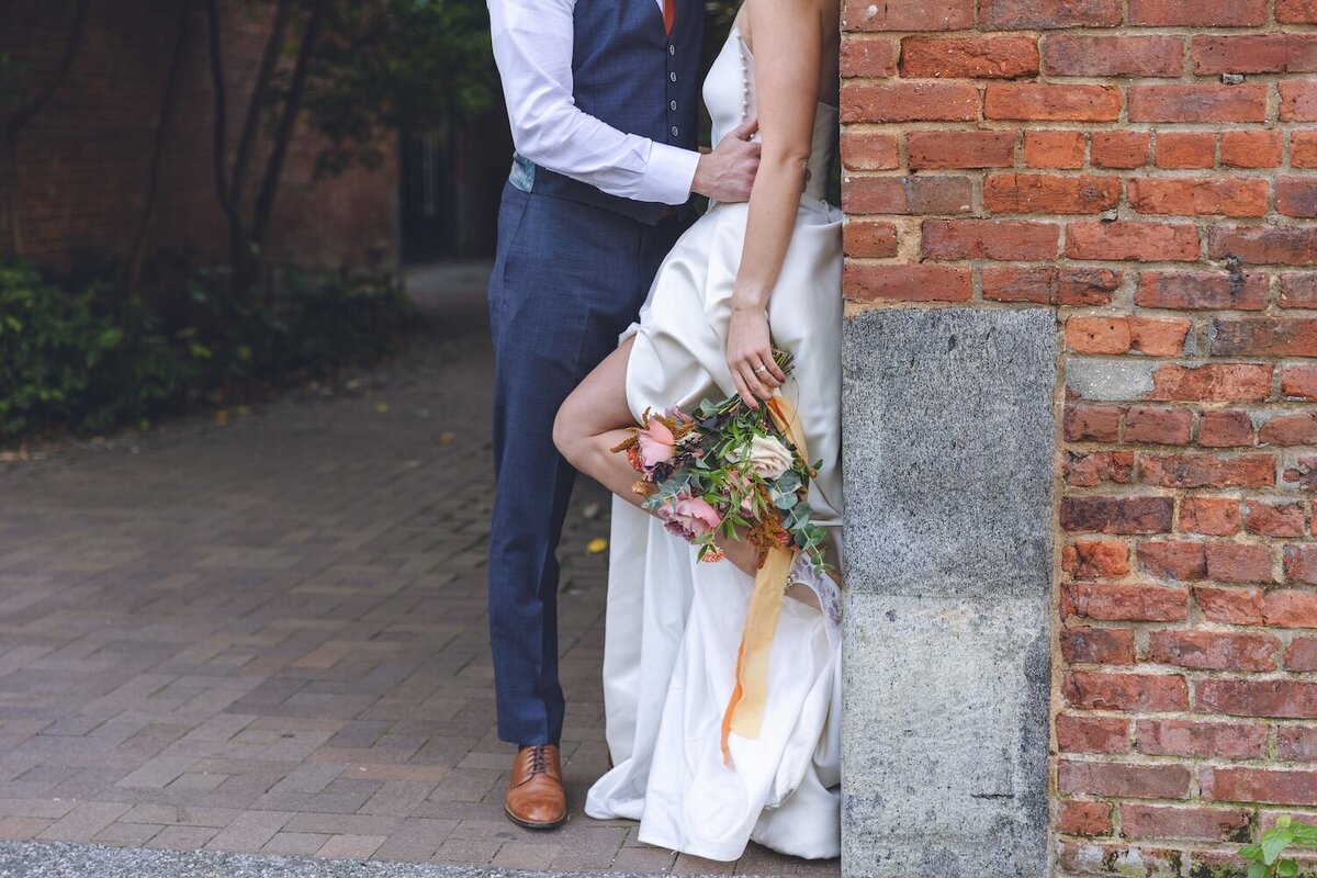 Groom and bride holding hands in front of brick wall