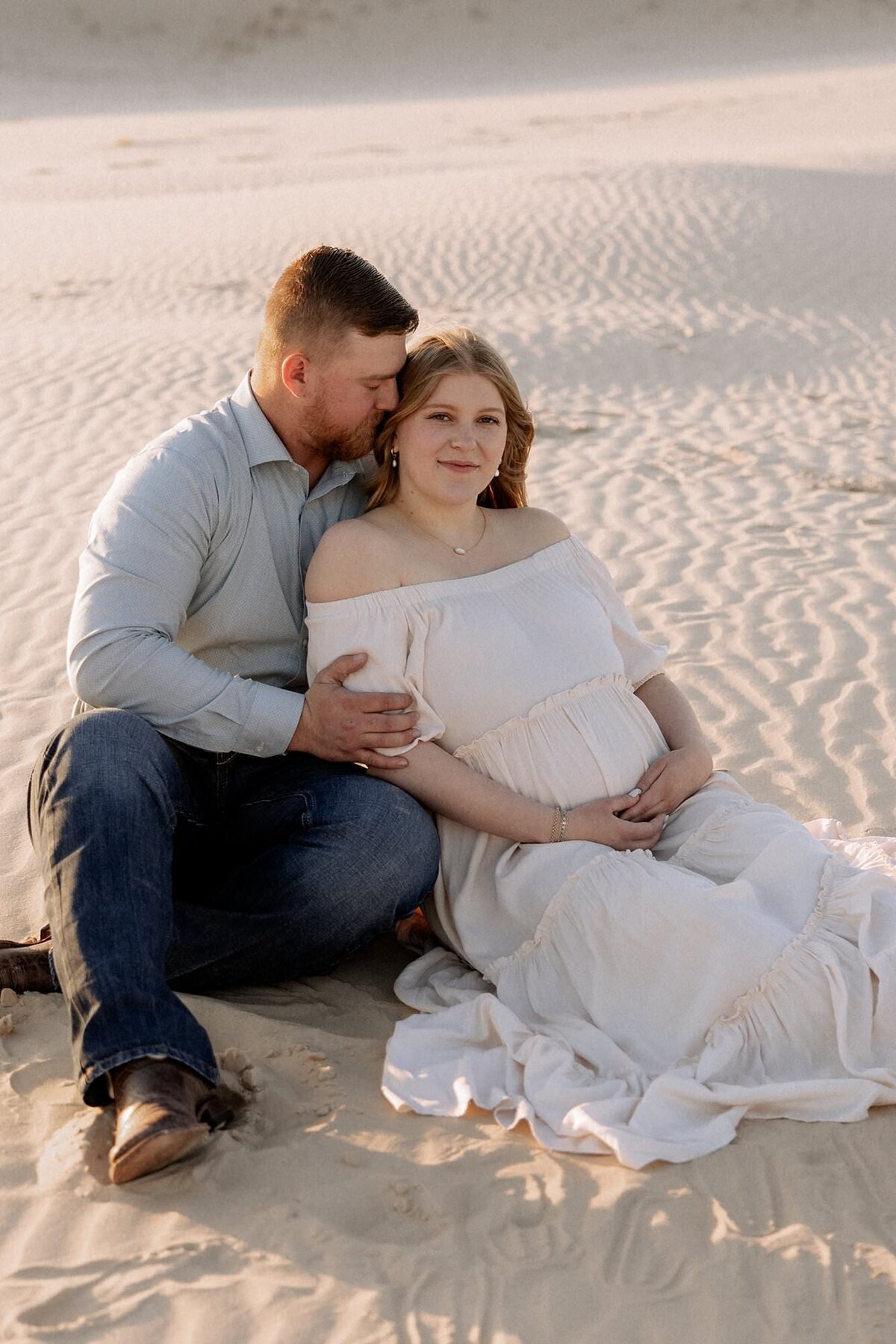 photo of maternity couple sitting in the sand enjoying their  time togehter