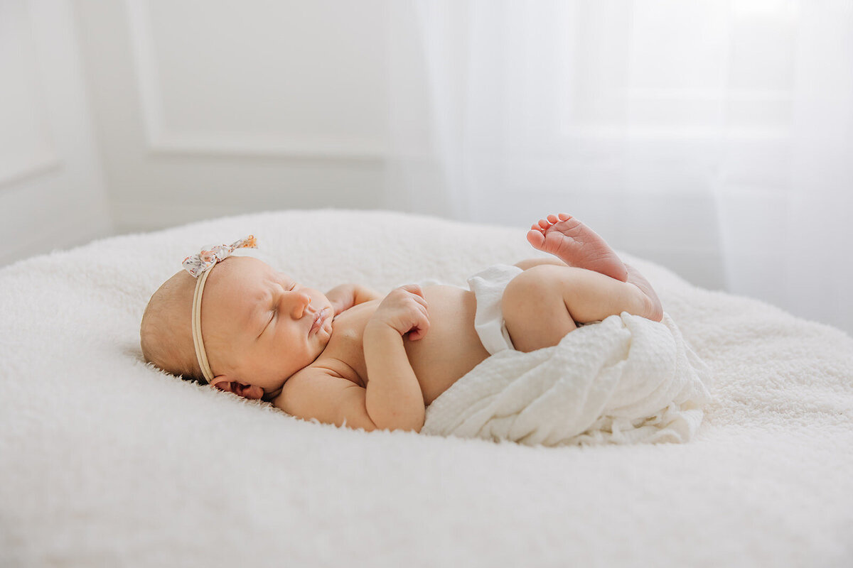 newborn girl laying on pillow next to window