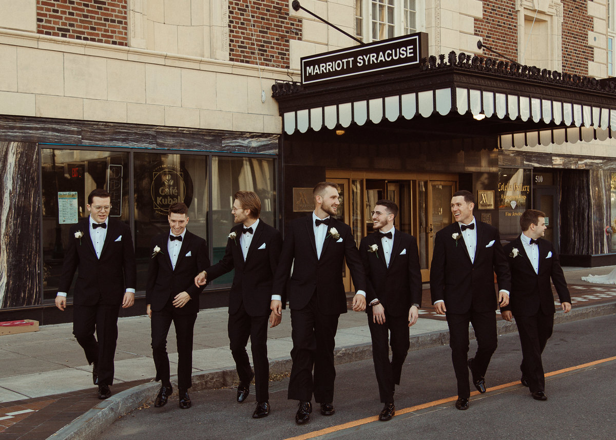 groomsmen walking with Hotel Syracuse behind them