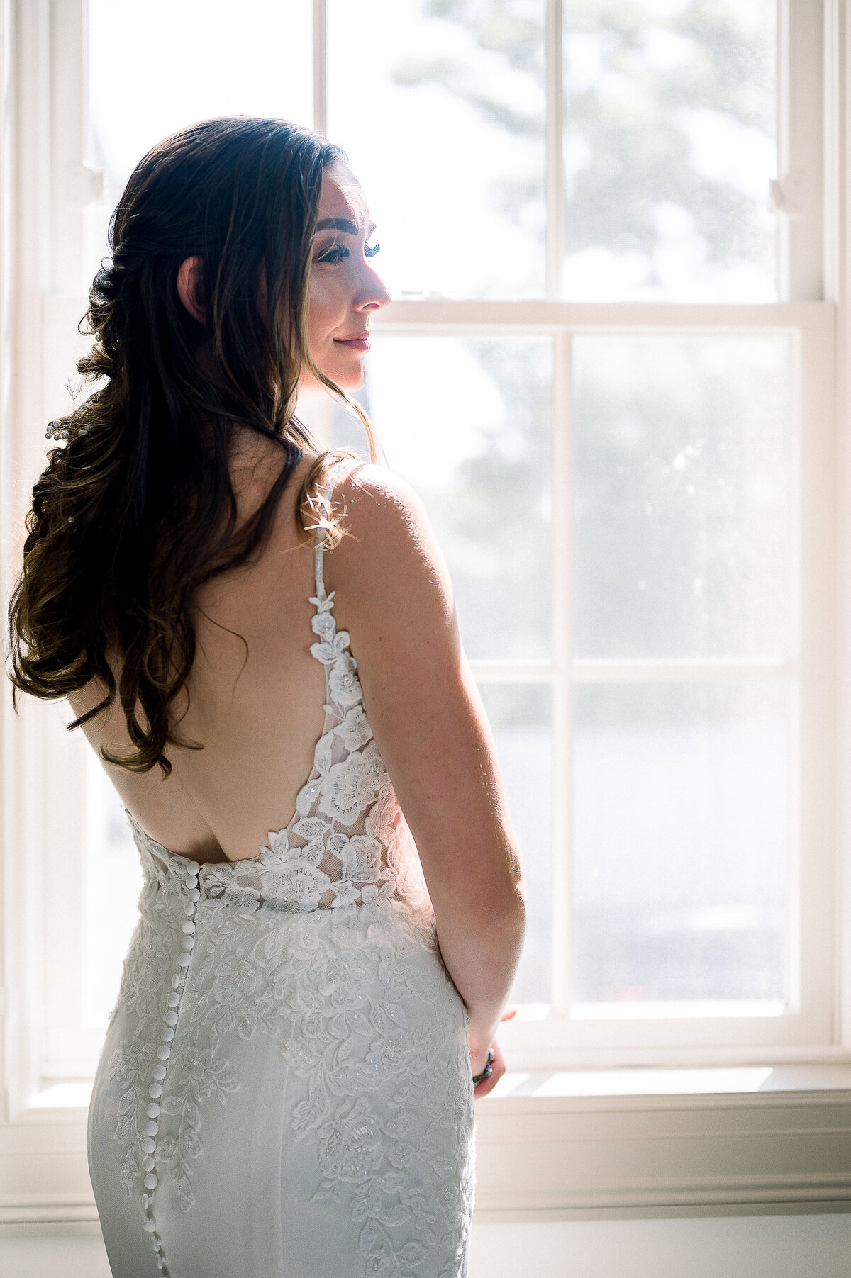 a bride standing near a window in her wedding dress
