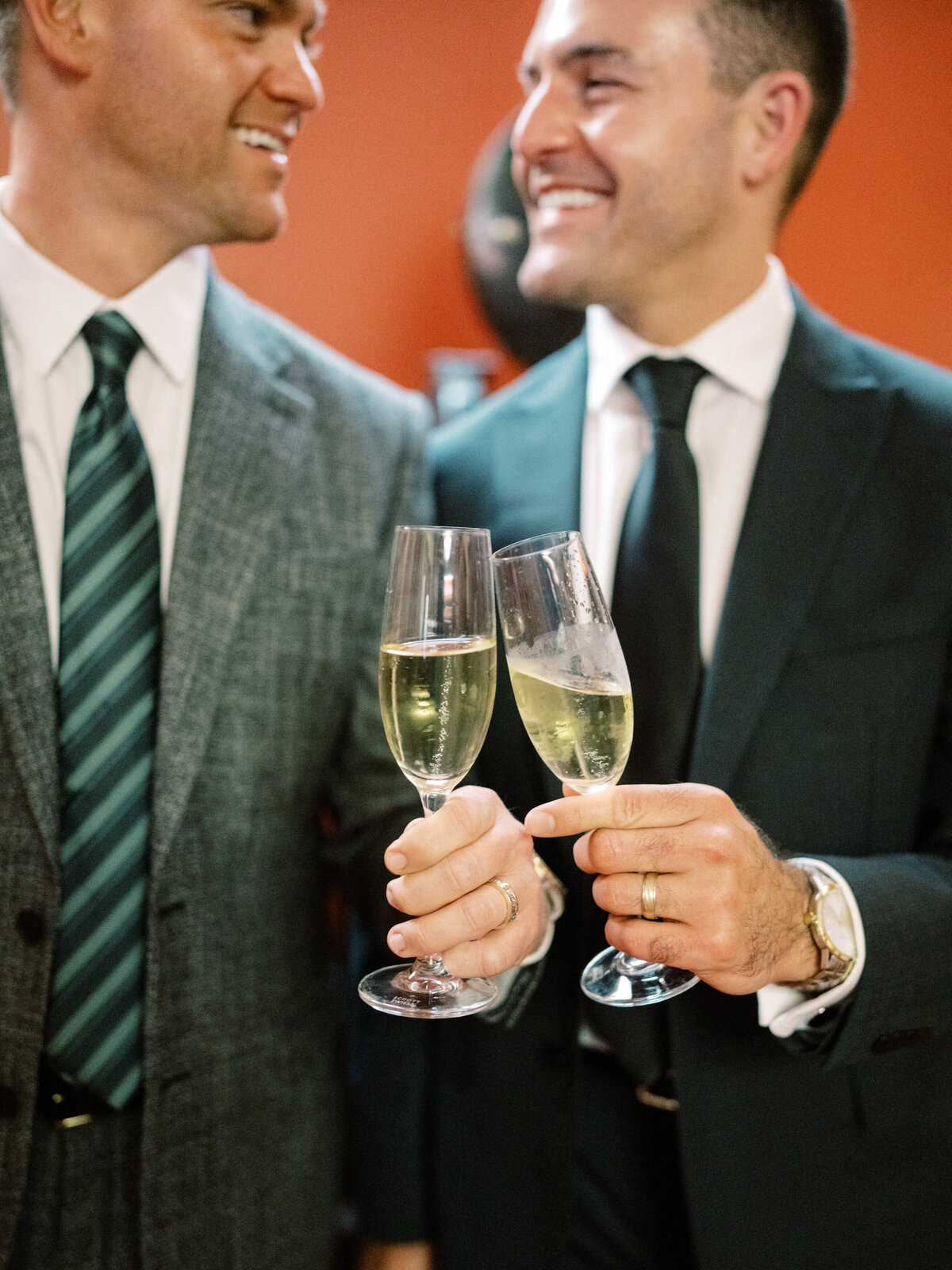Two smiling men raise their champagne glasses in a toast, celebrating friendship and love at an elegant wedding occasion full of joy and happiness.