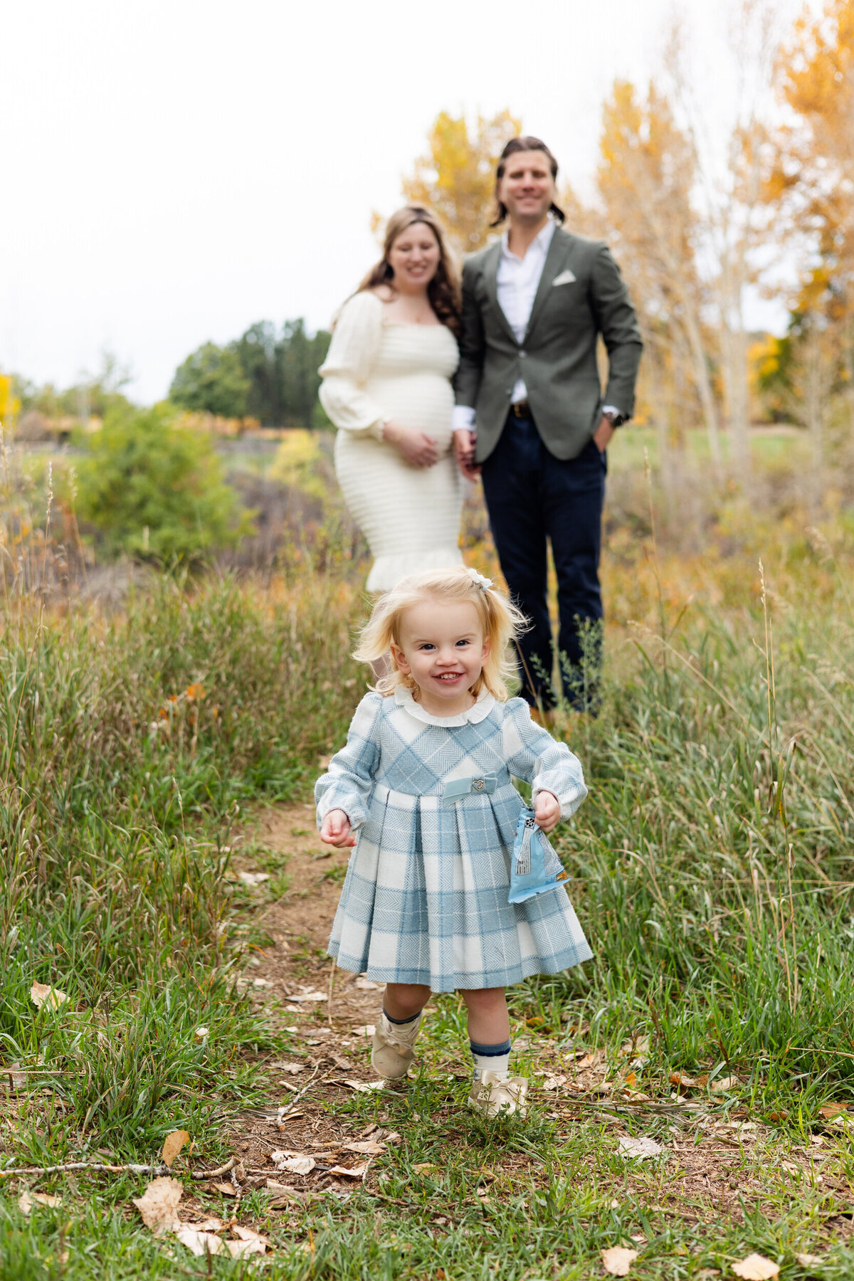 Toddler girl laughs and runs away from parents with snack bag.