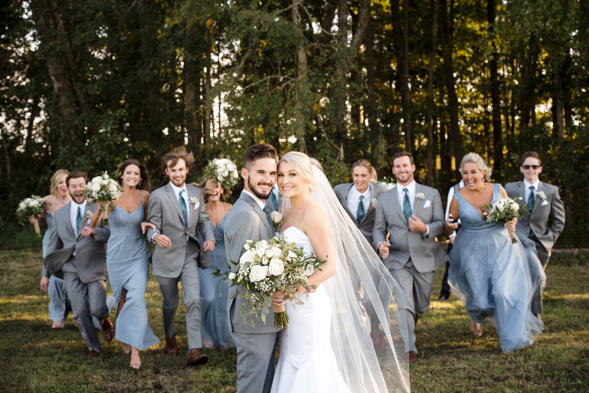 Wedding party running to bride and groom from behind for a surprise hug at Dove Meadows Estate by Charlotte wedding photographer DeLong Photography