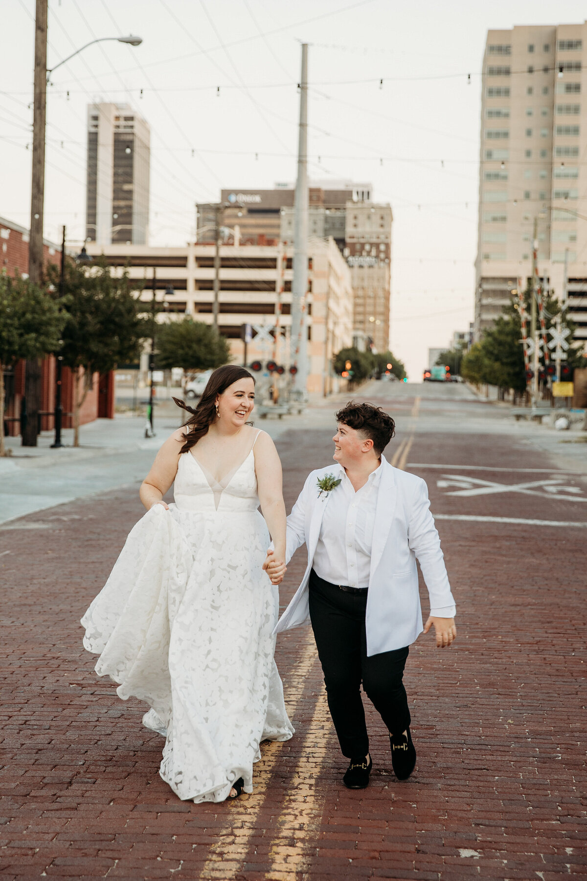 Two brides smiling and walking hand in hand down an urban street