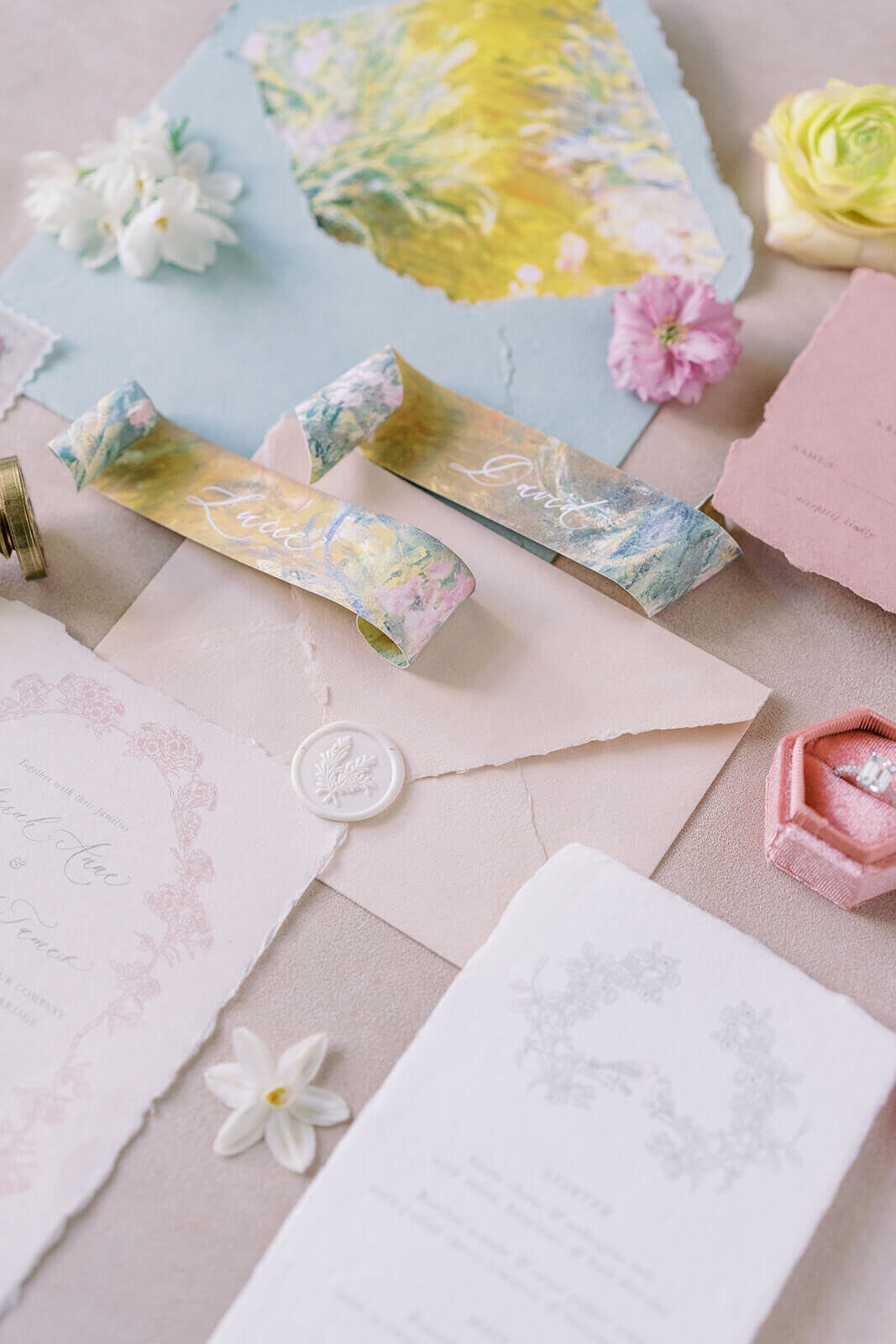 flat-lay of pink and blue wedding stationery on natural paper with floral patterns displayed with a ring and flower heads for a wedding at blenheim palace
