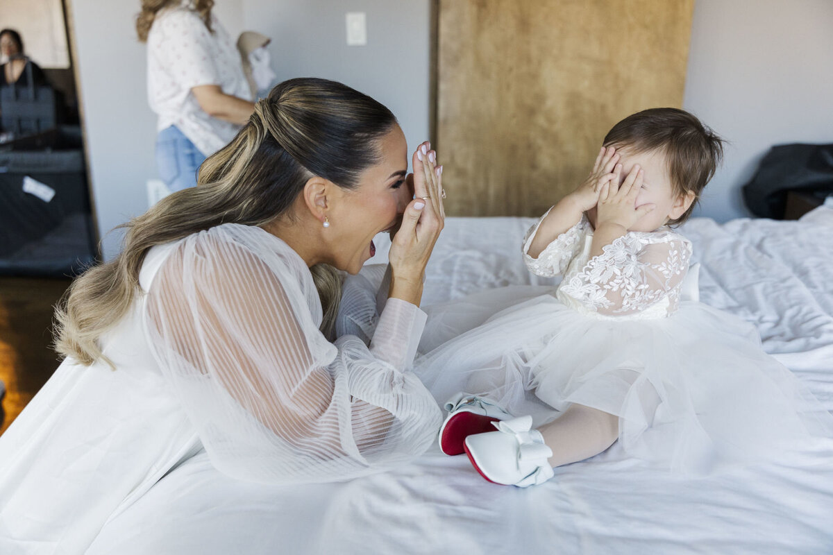 Candid getting ready photo of a bride playing peekaboo with her flower girl