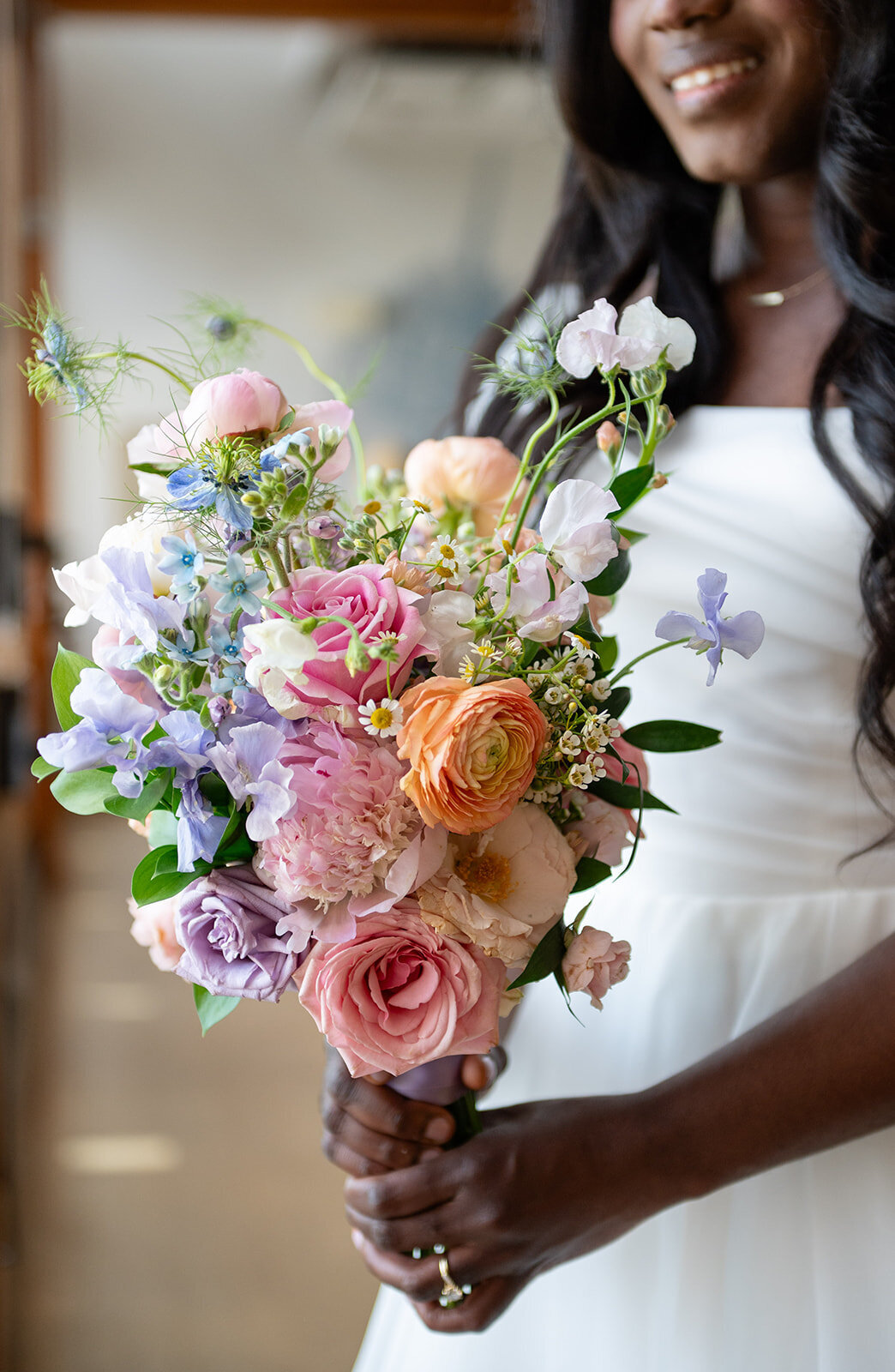 Lush and colorful bridal bouquet featuring peach, pink, blue and lavender blooms with accents of greenery.