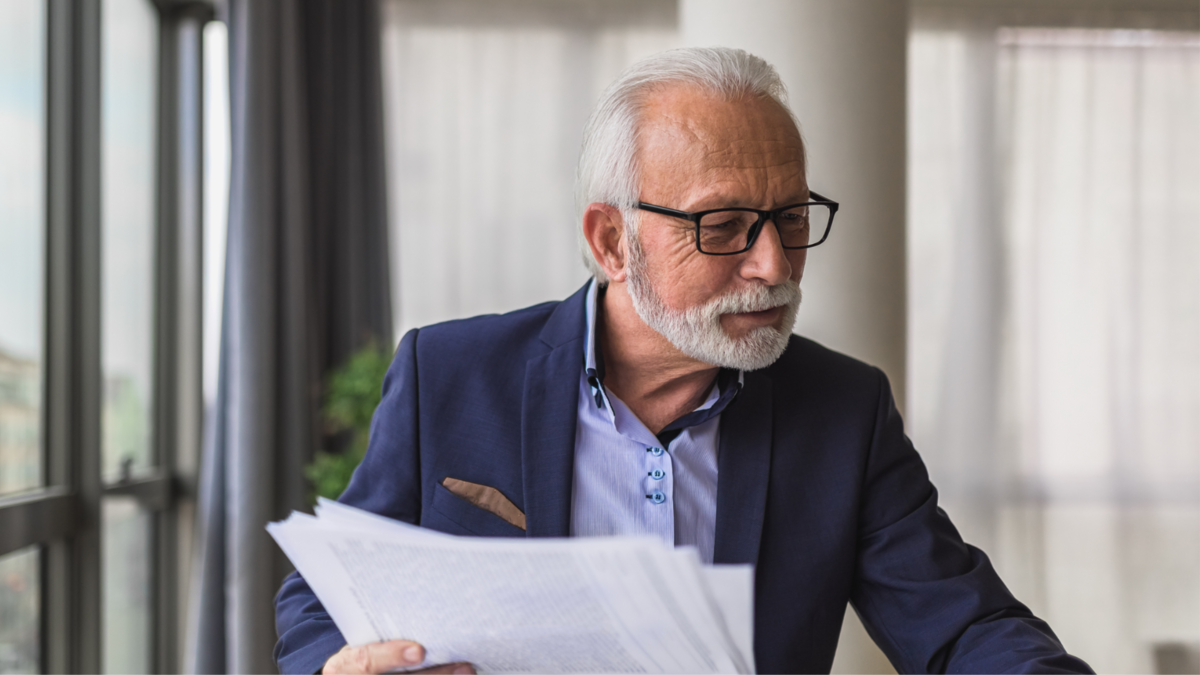 Mature businessman analyzing documents by a window—representing experienced business owners preparing to sell their companies with guidance from Meritus Group

