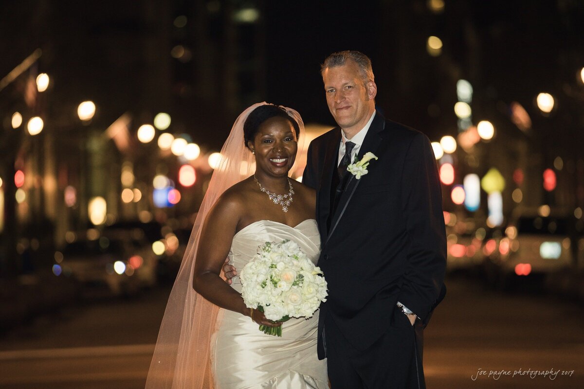 A wedding couple smiling while standing in the middle of the street together.