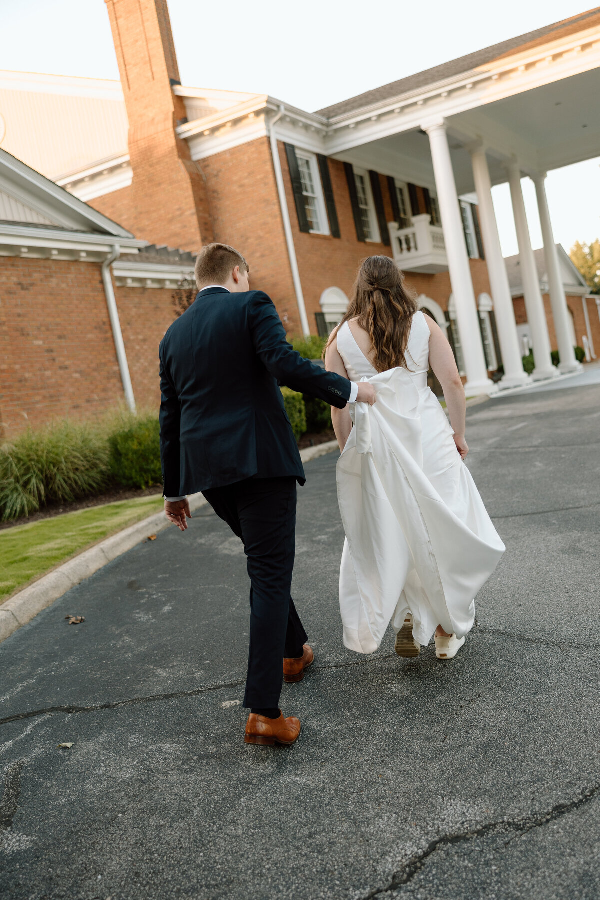 Groom assists bride with her train as they walk into Holly Tree country club for their wedding reception