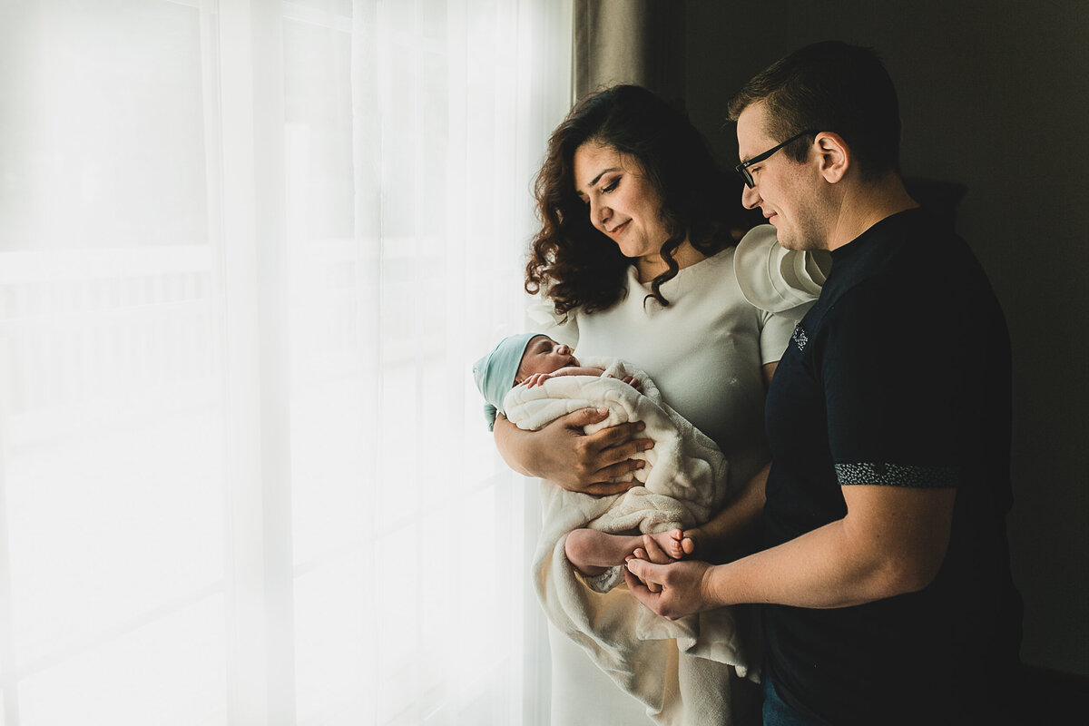 Mom holding new born baby, with dad holding arms around mom.
