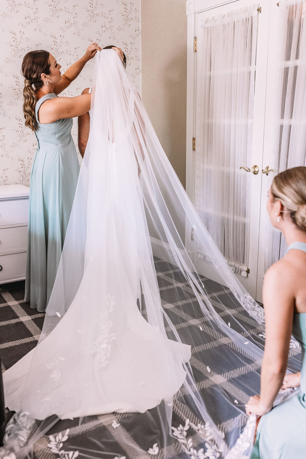 Maid of honor putting the cathedral length vail on bride in getting ready room at Wentworth Inn in Jackson NH by Lisa Smith Photography