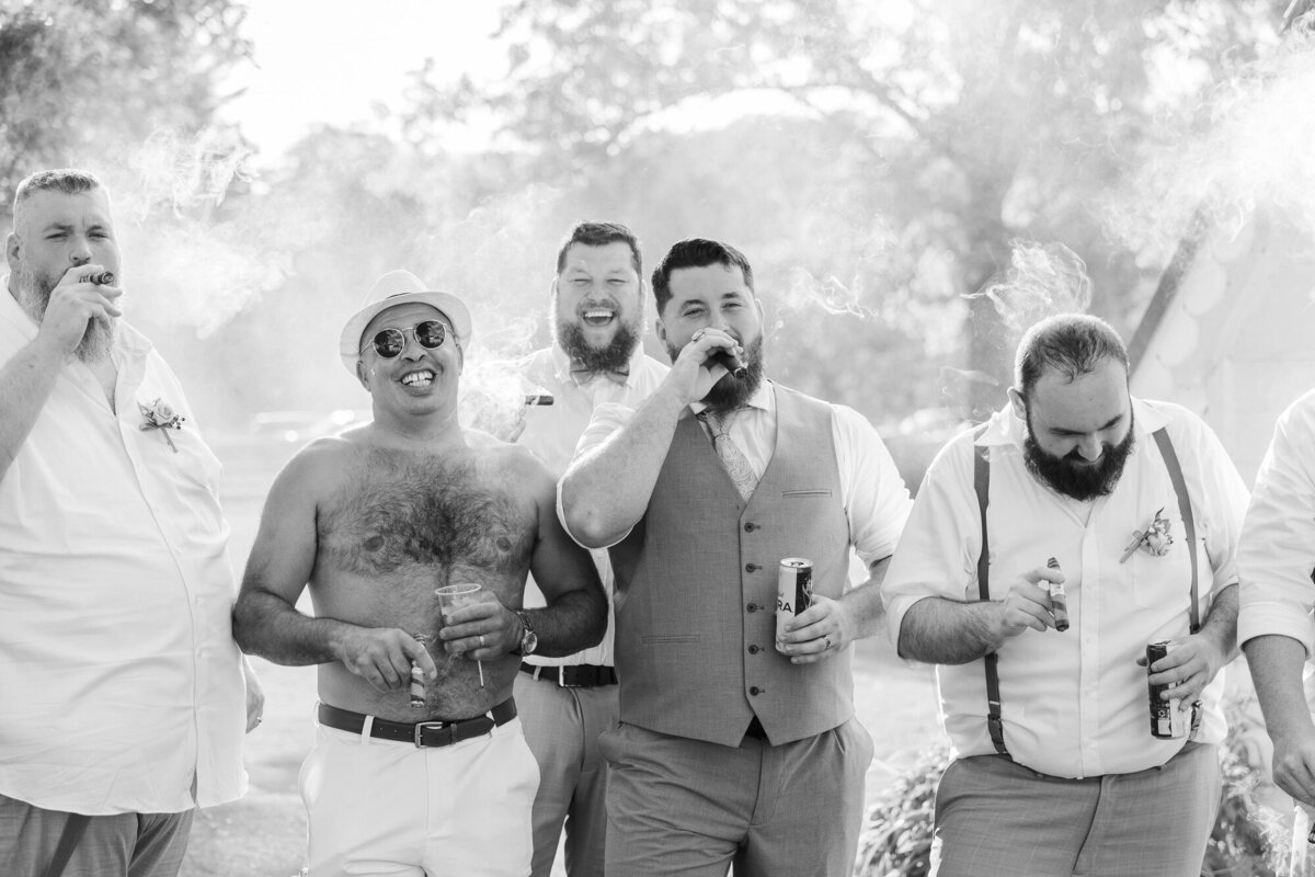 Black and white photo of groomsmen laughing and holding drinks on a sunny lawn