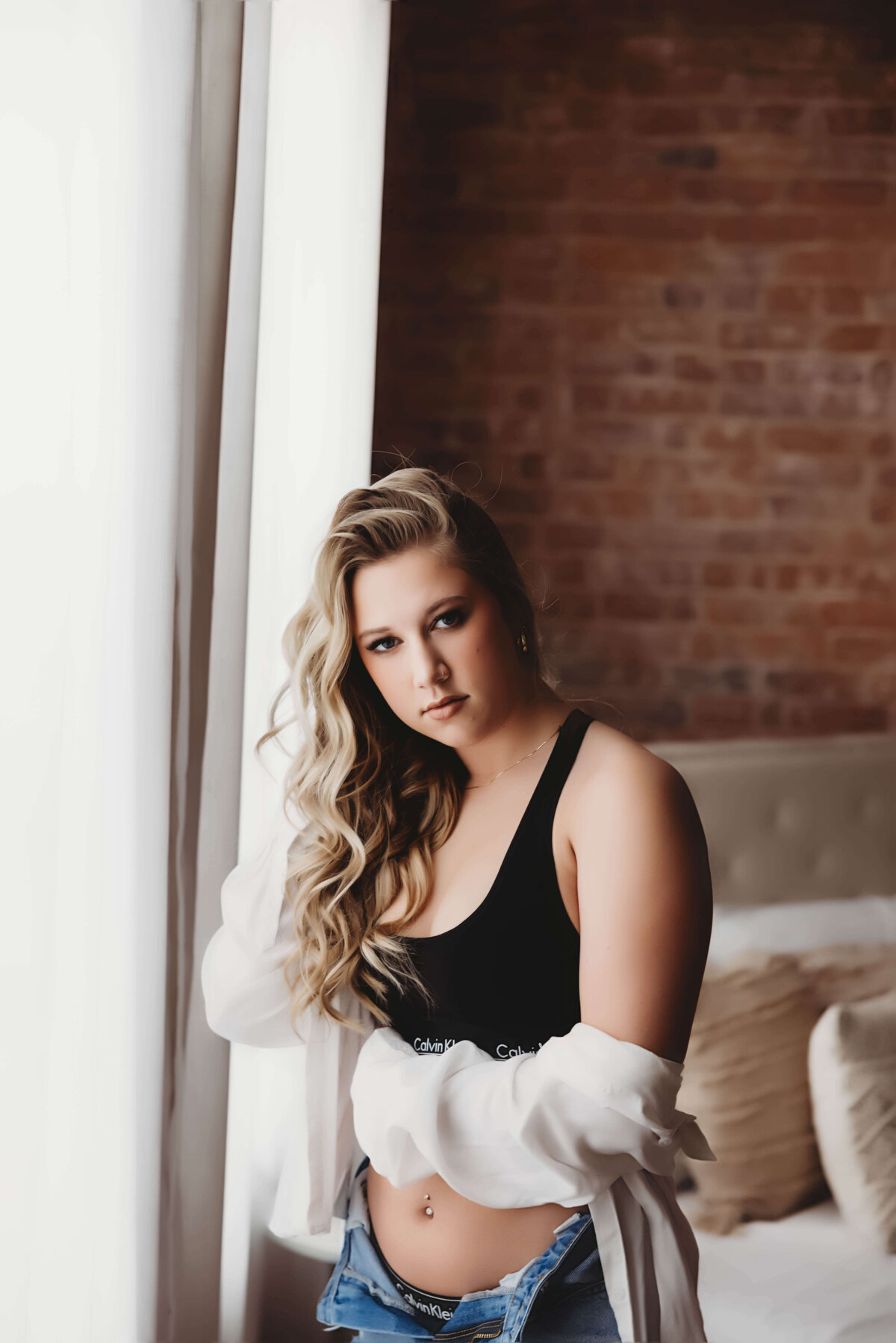 Woman standing by window in Calvin Klein and jeans for boudoir session with Reva Davis photography