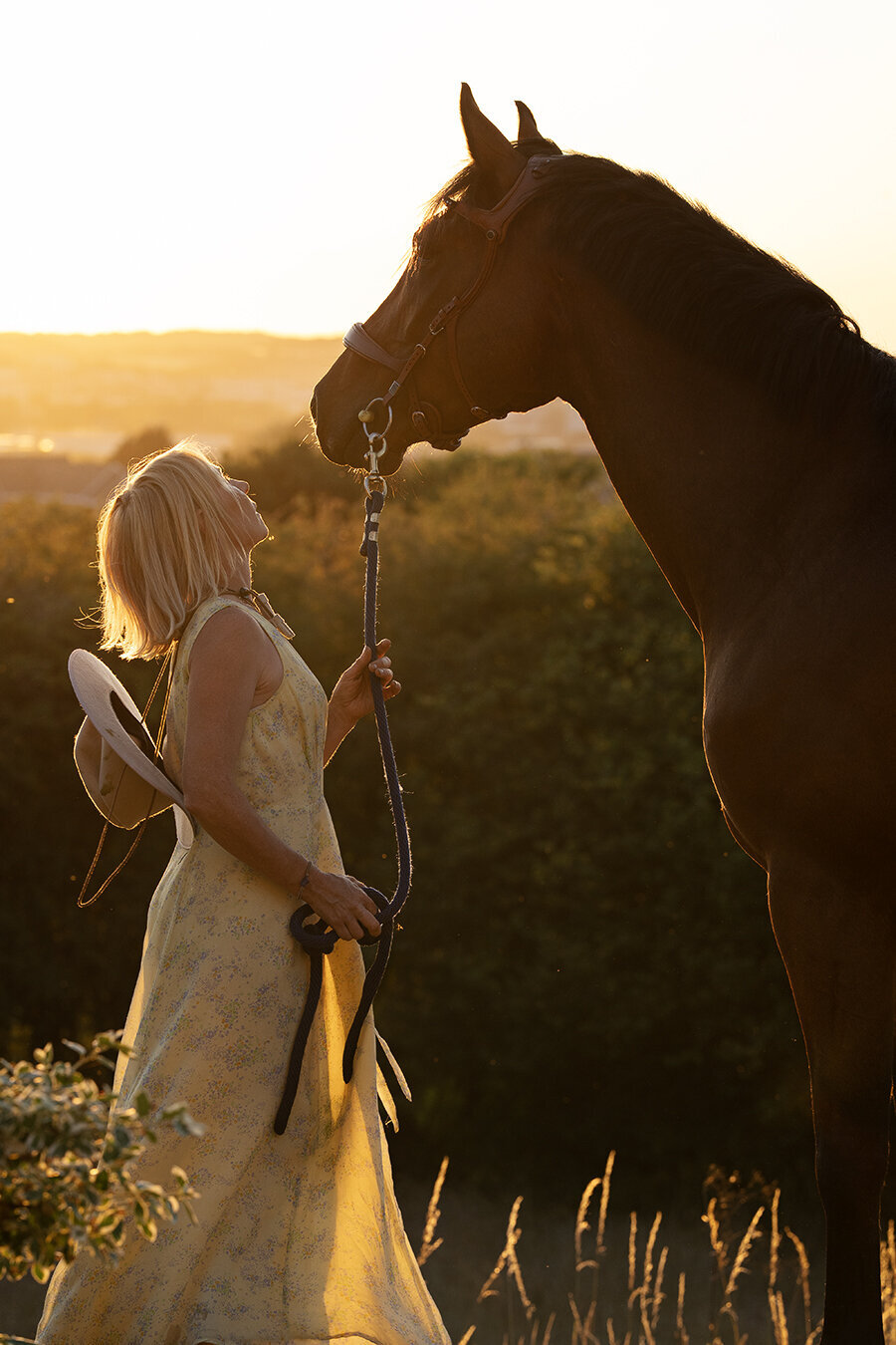 a women in a yellow dress is kissing her horse at sunset