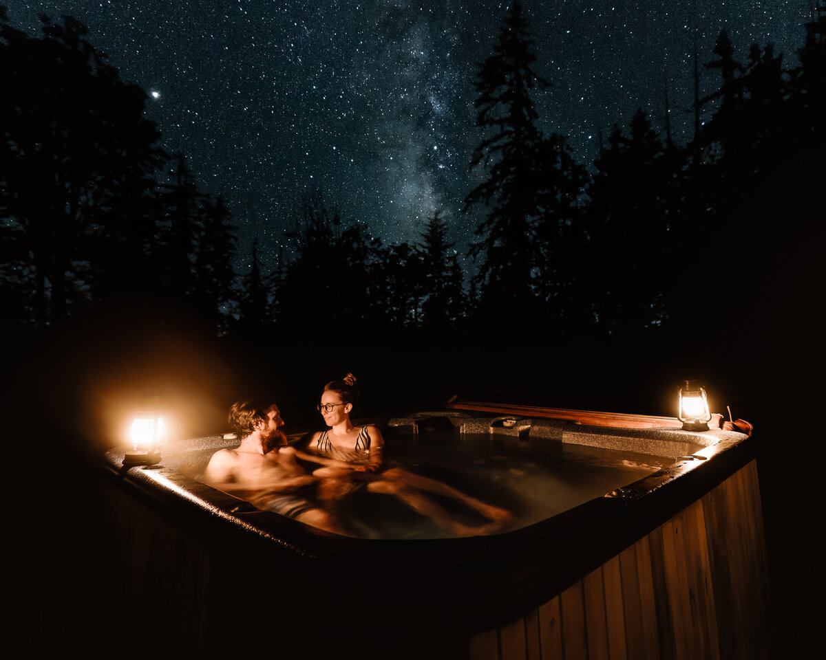 A couple soaks in a hot tub beneath the milky way, lit only by lanterns and moonlight, ending their Olympic National Park wedding day