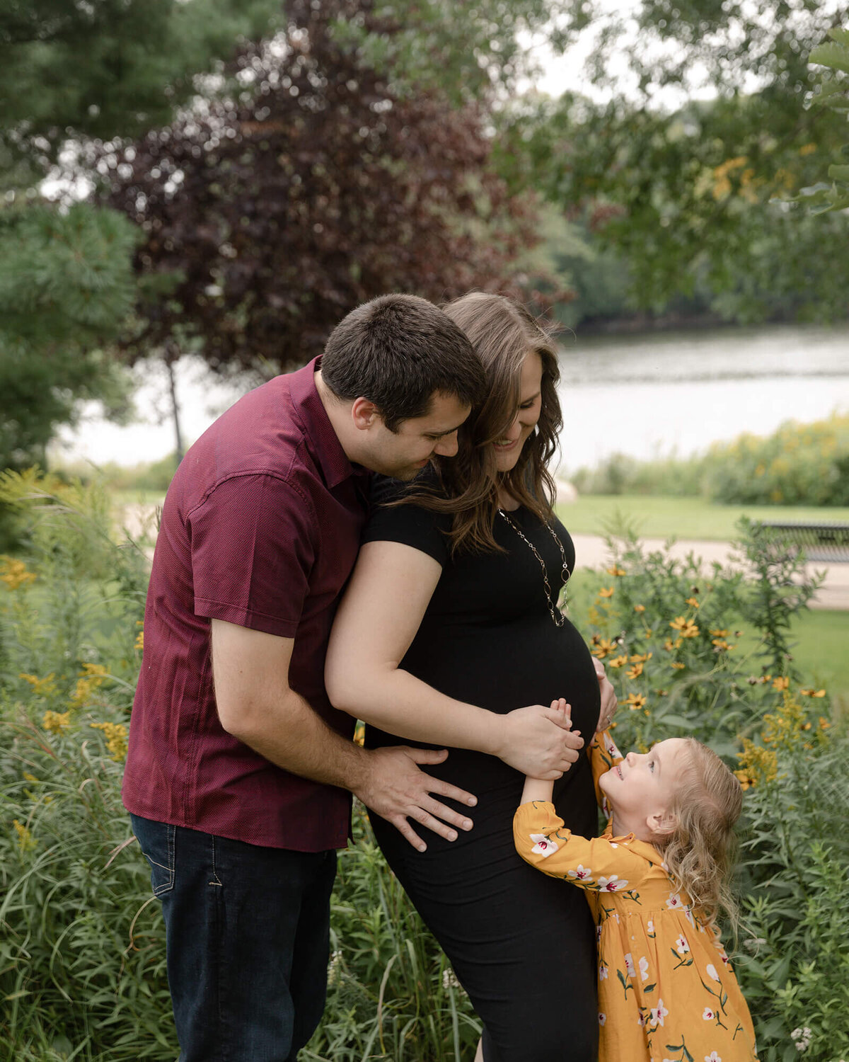 Dad kissing his pregnant wife while their little girl touches Mom's belly.