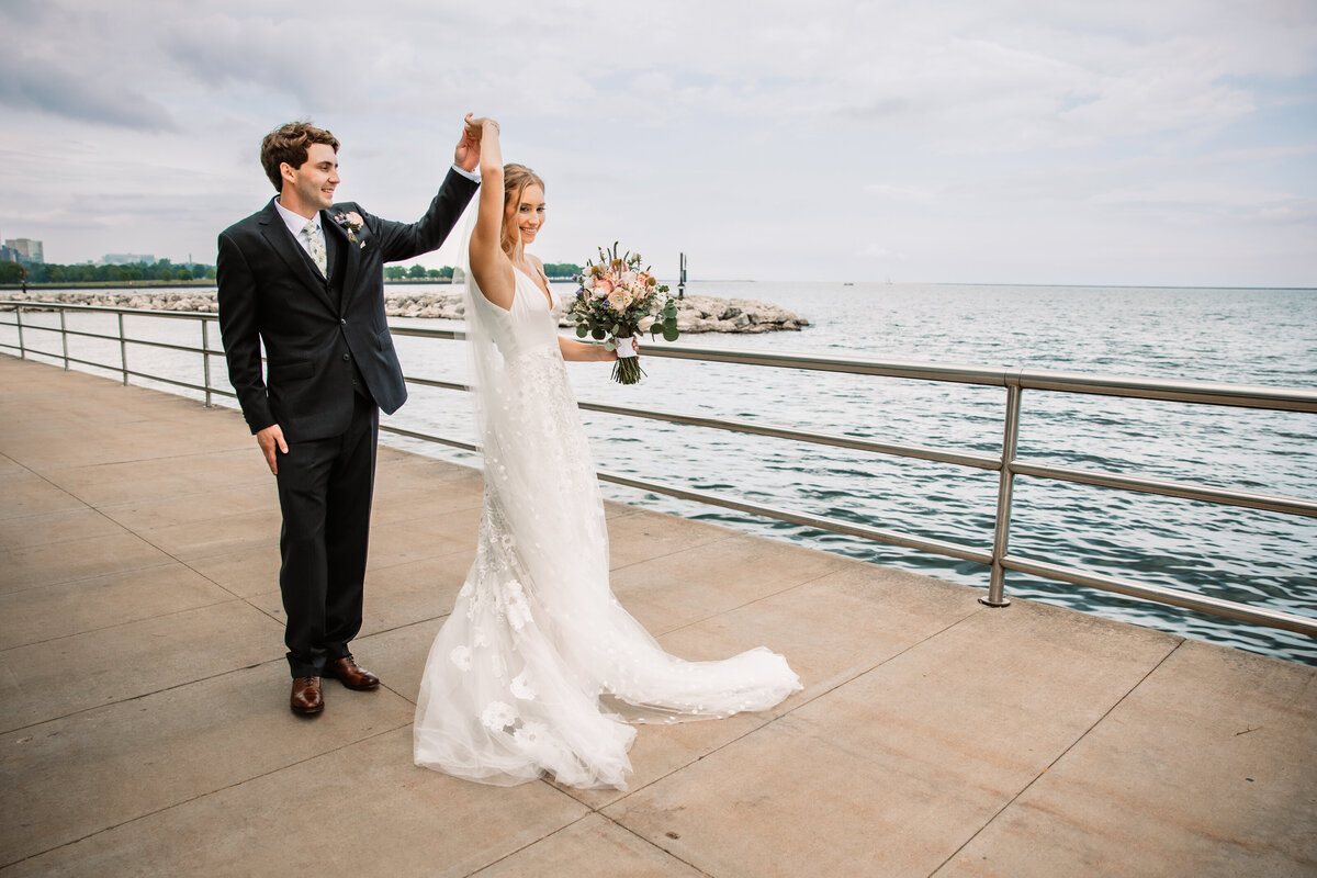 Newlyweds dance by the water as the bride spins with her bouquet