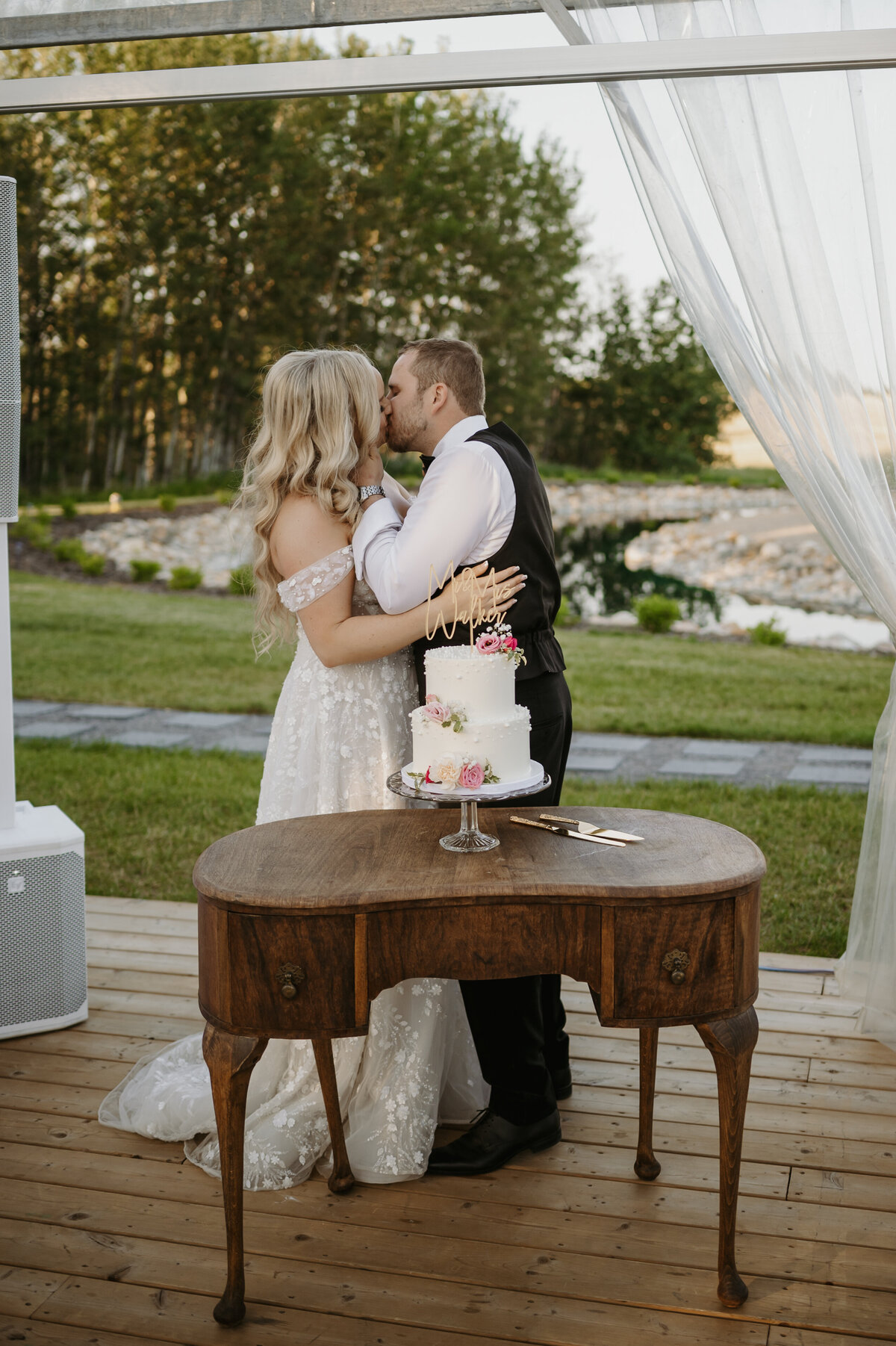 couple kissing as they cut wedding cake 