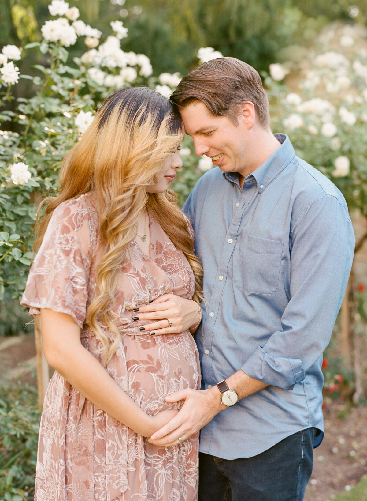 New parents look lovingly at mom's pregnant belly during a maternity session at the Raleigh Rose Garden. Image by Raleigh maternity photographer A.J. Dunlap Photography.