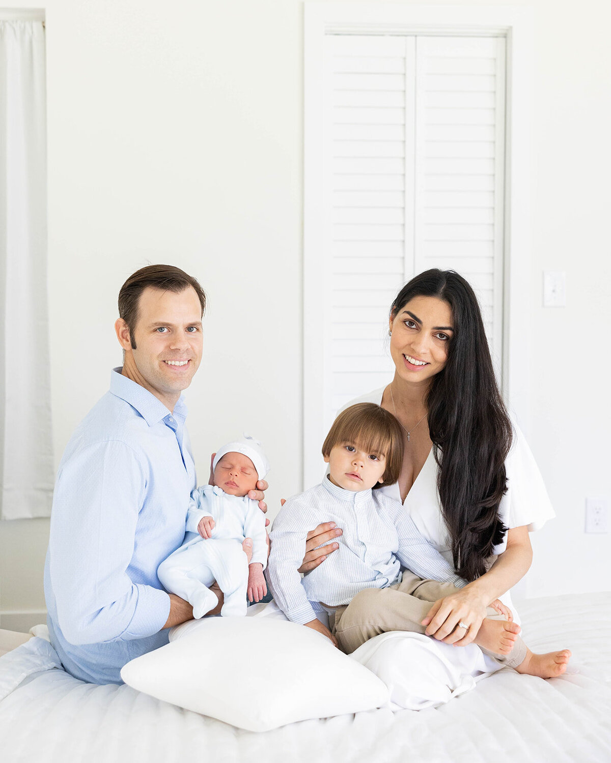  A stylish family of four sits on a bed together in their home, taken during an intimate Florida Keys family session by Claudia Amalia.