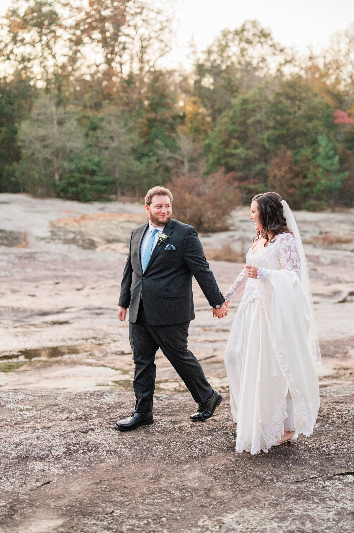 A newlywed couple holding hands and smiling while walking outside
