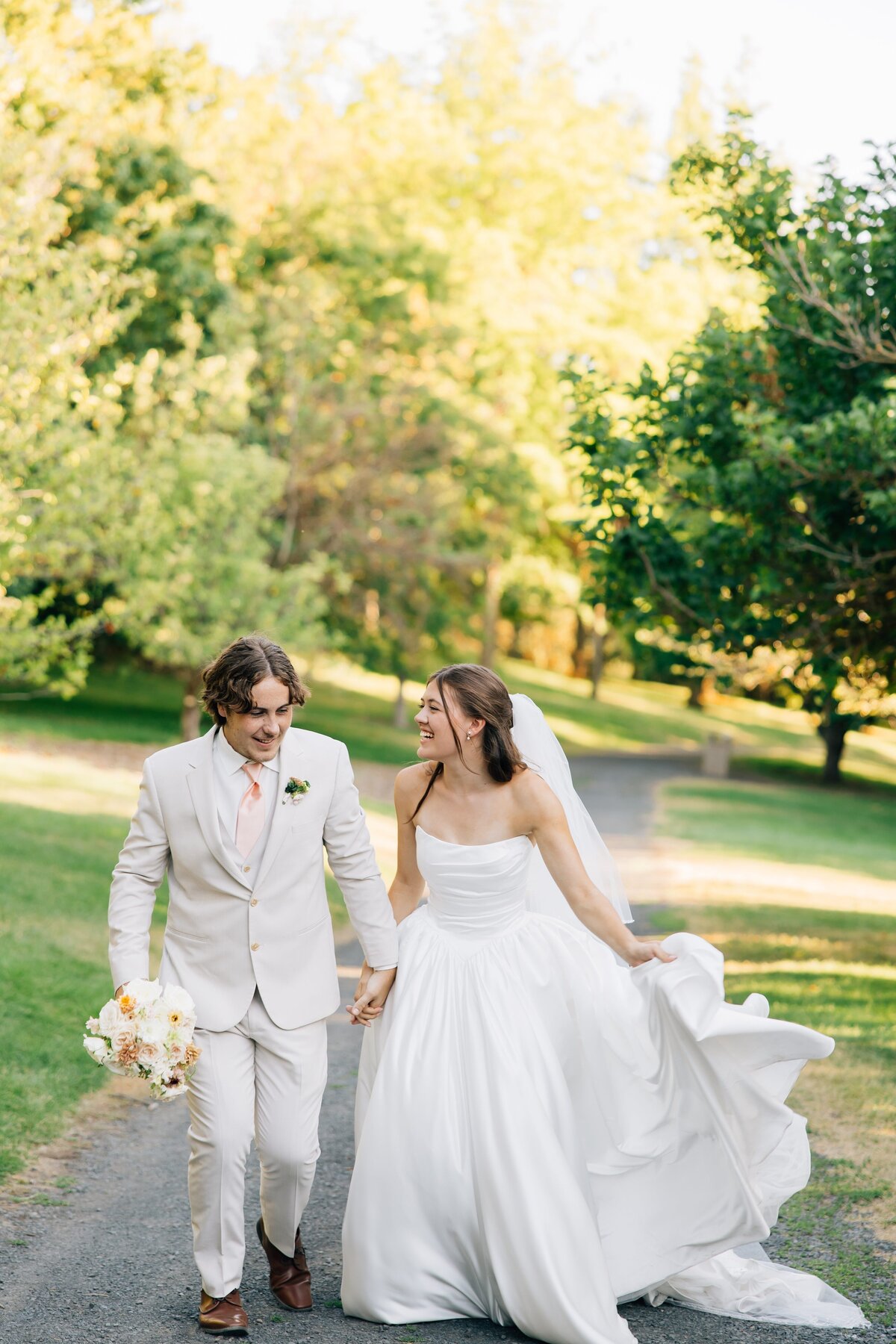 Bride & Groom running amongst green trees and pathway smiling at each other right after they got married
