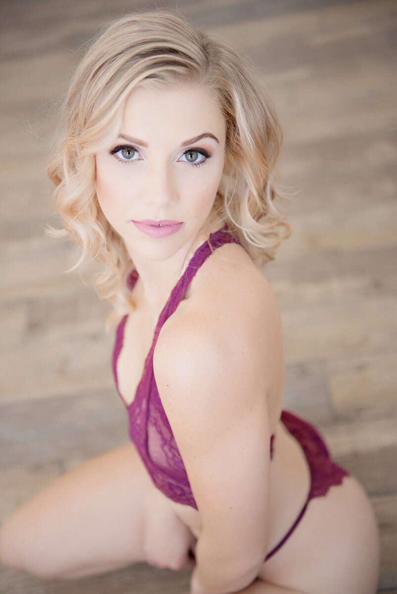 A stunning portrait of a blonde woman in purple lingerie, showcasing her beauty and sensuality in a seductive and alluring way. Captured in a boudoir setting, this image exudes confidence and grace, perfect for anyone looking for a touch of elegance and sophistication in their boudoir experience.
