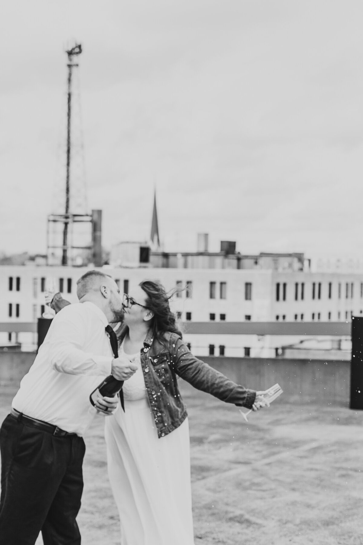 BRIDE AND GROOM CELEBRATE THEIR WEDDING IN DOWNTOWN  CANTON OHIO ON THE ONESTO ROOFTOP WITH A KISS AND A BOTTLE OF CHAMPAGNE TOGETHER IN CLASSIC BLACK AND WHITE