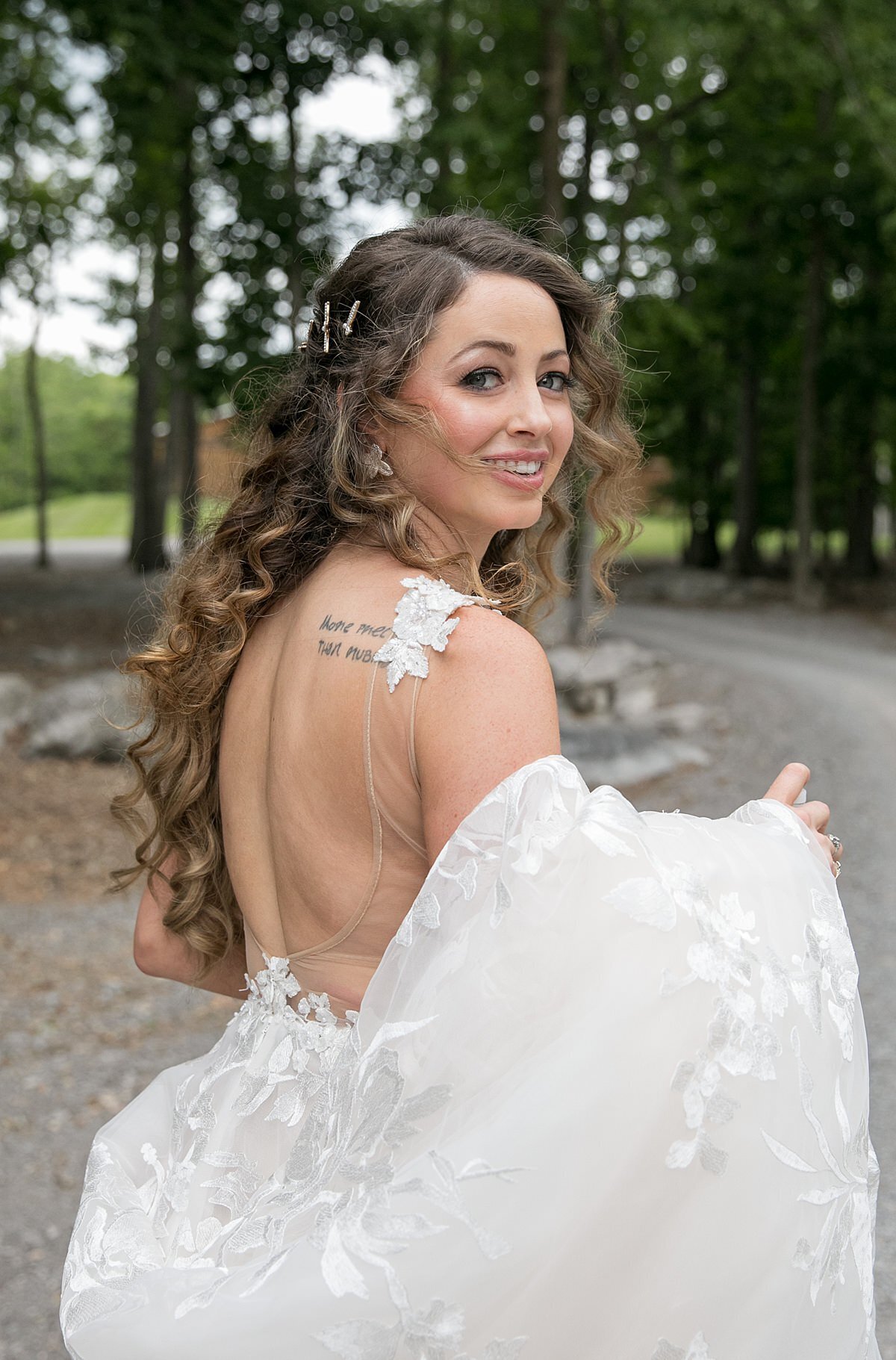 Bride in a backless lace wedding dress walks down the wooded pathway at Saddle Woods Farm.