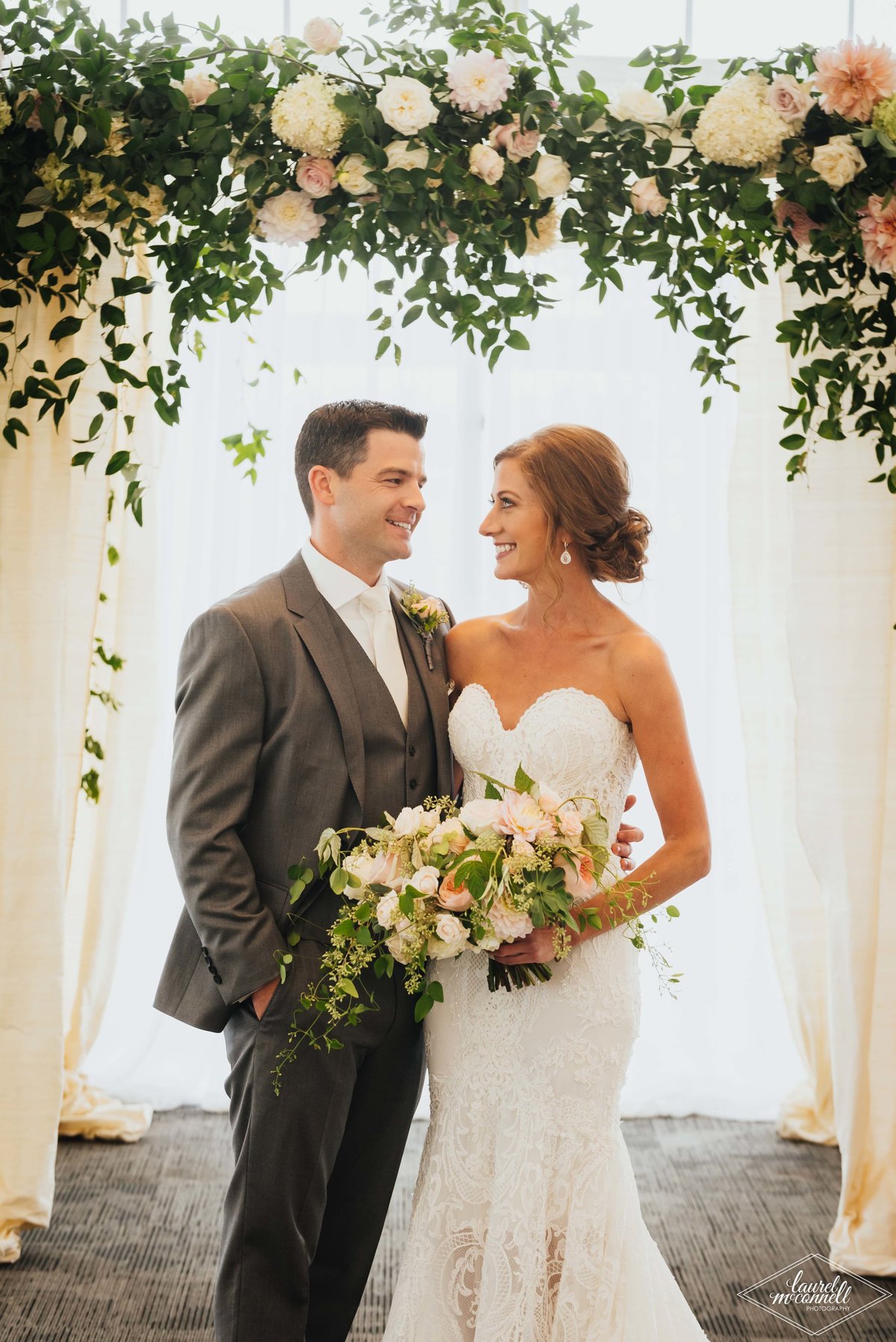wedding couple standing underneath greenery chuppah, and bride holding garden flower bouquet